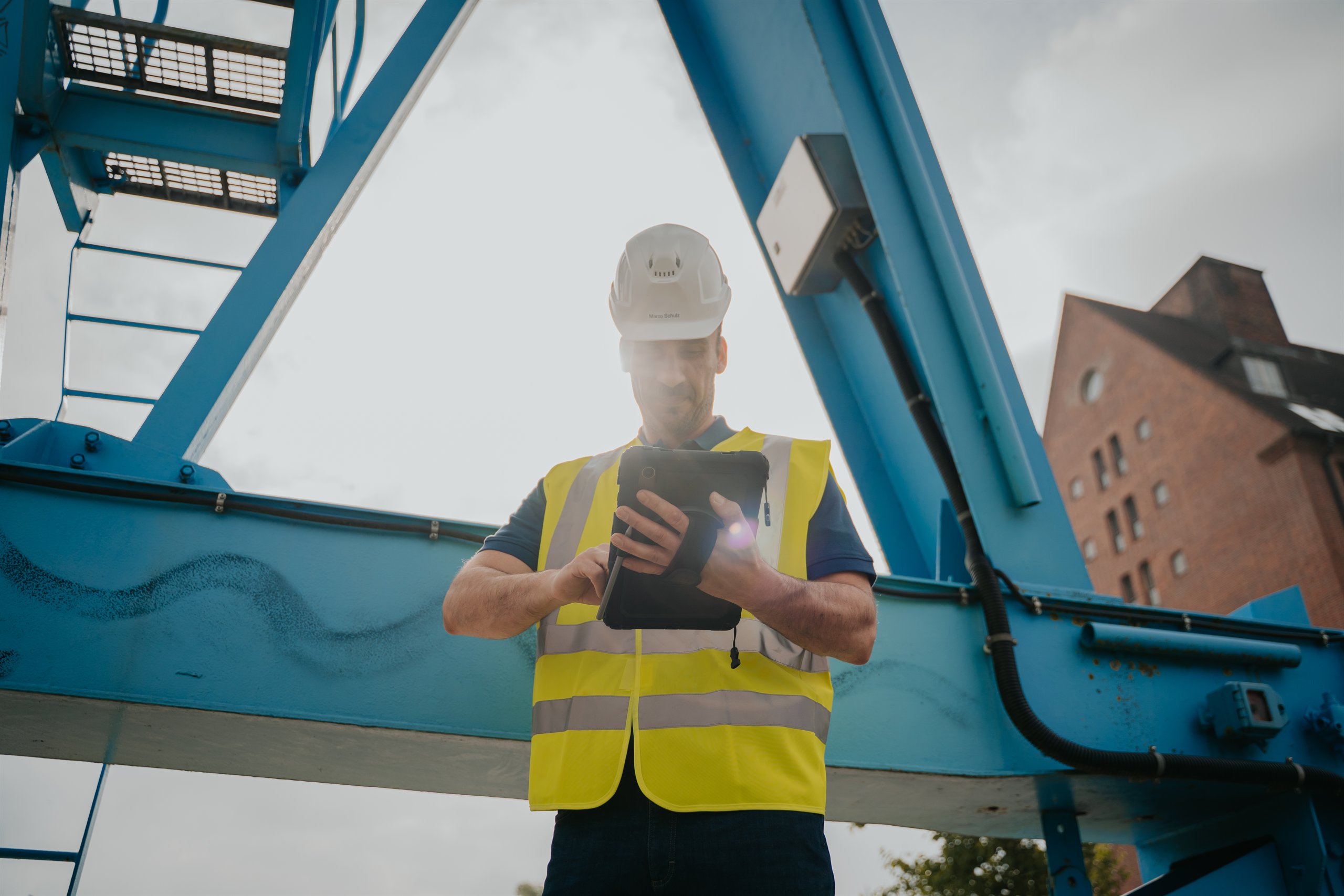 Sicherheitsfachkraft mit Helm und Warnweste prüft Anlagen auf einem Industriegelände